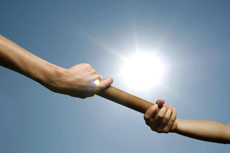 Hands passing a baton under sunlight