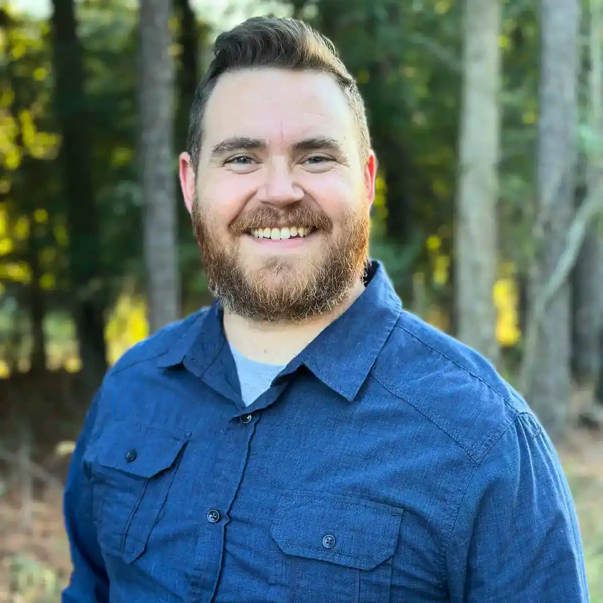 Ryan Mulvaney smiling outdoors in a blue shirt with a forest background.